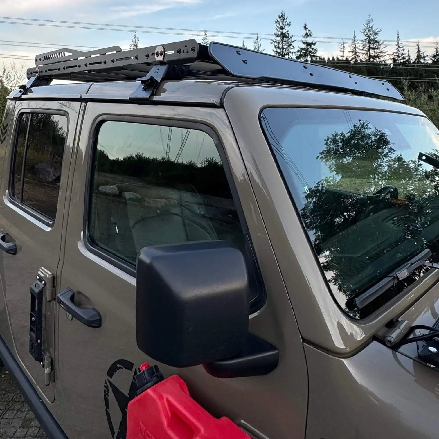 Jeep Gladiator with a roof rack and side mirror, parked outdoors with trees in the background.