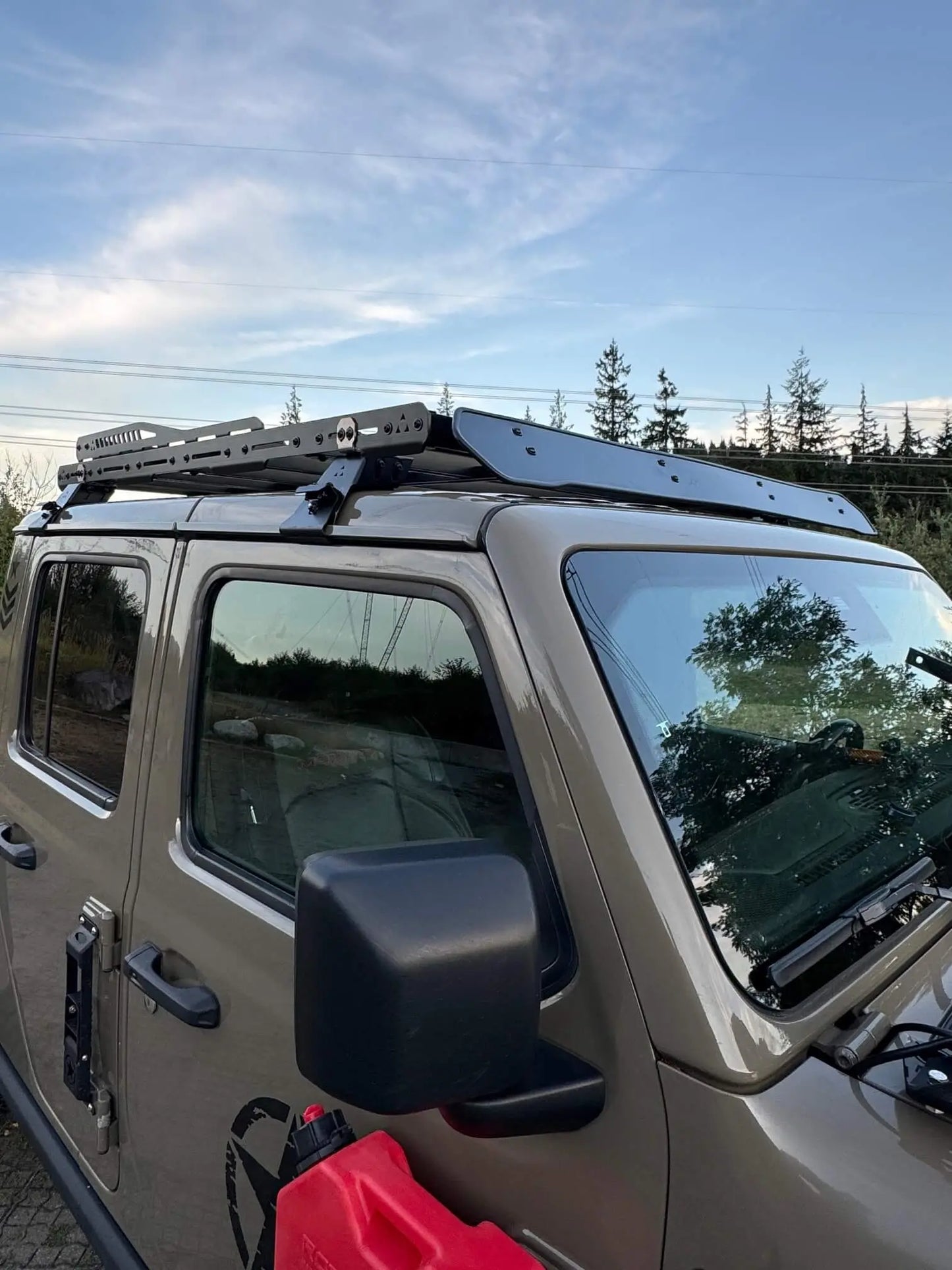 Jeep Gladiator with a roof rack and side mirror, against a clear sky.